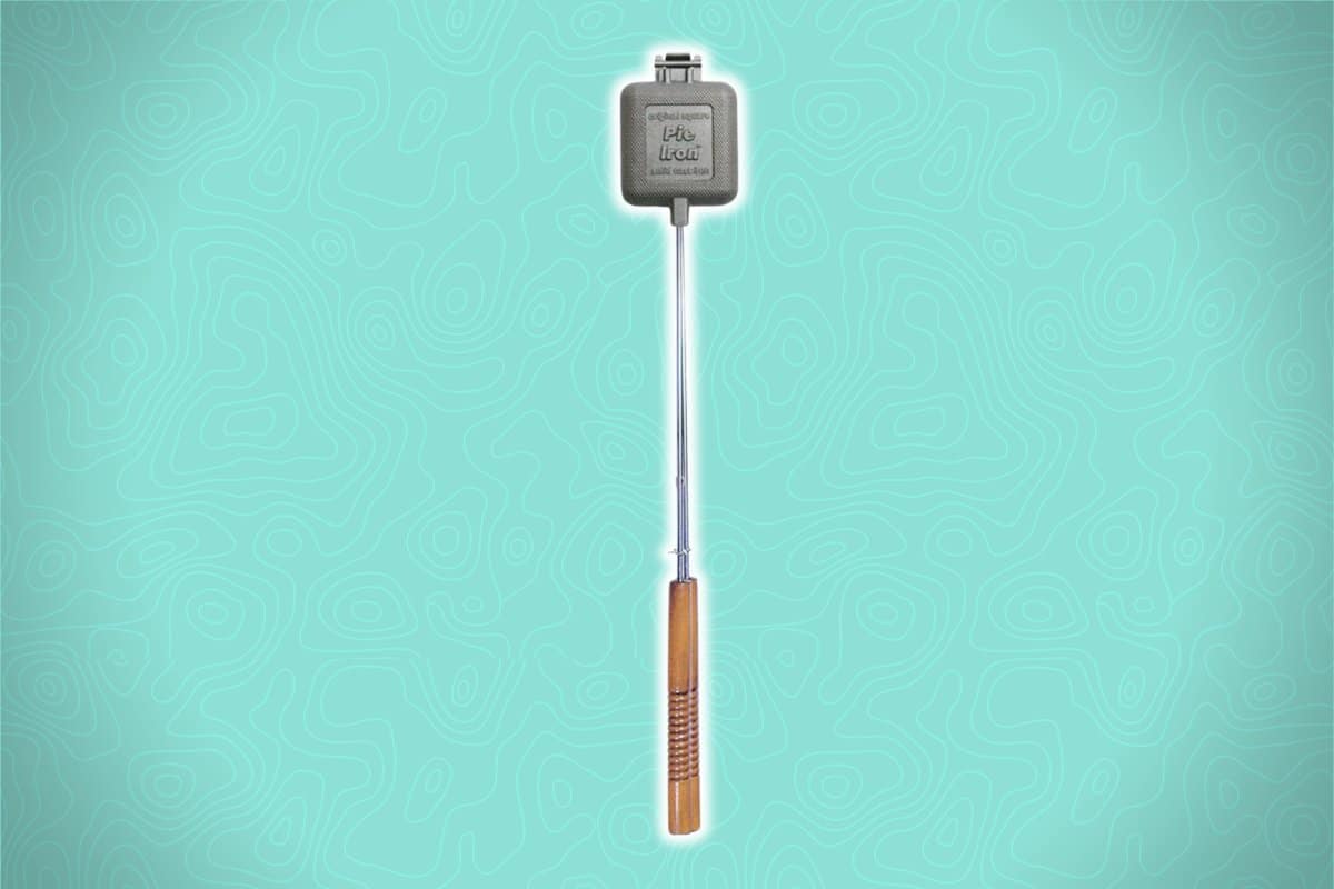 A branded grilling iron with a wooden handle rests against a teal background with a subtle abstract pattern, displaying a logo and grilling instructions on its metal top.