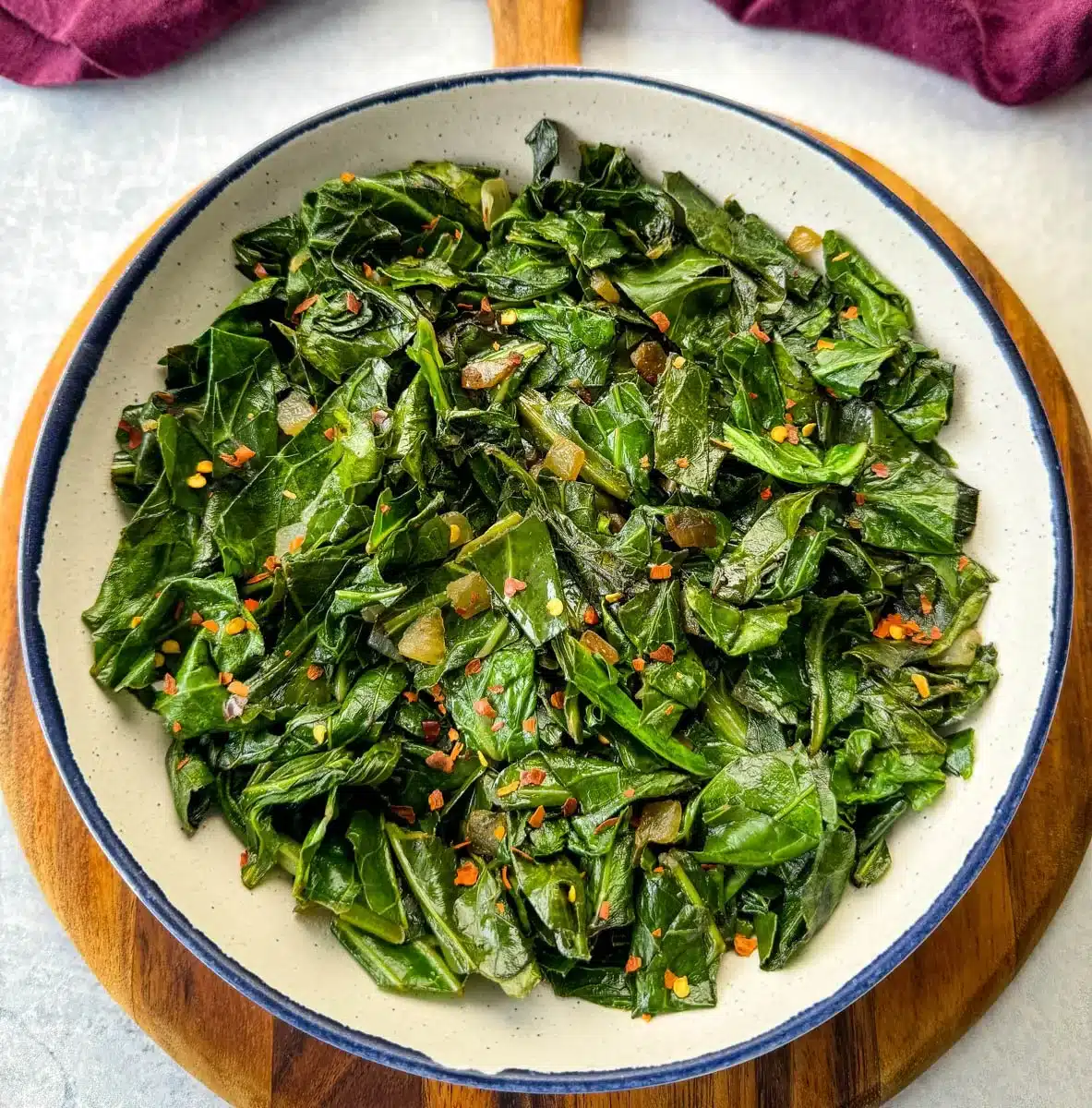 A plate of collard greens, seasoned with garlic and red pepper flakes, is displayed on a wooden board against a rustic background.