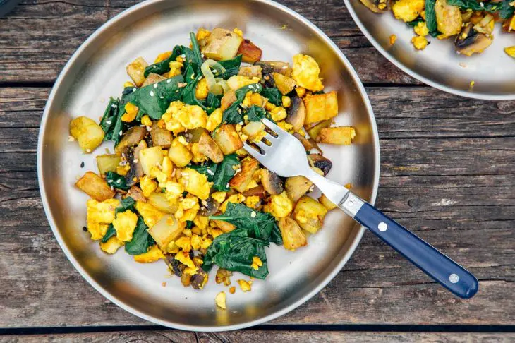 Overhead horizontal photo of a tofu scramble with spinach on a silver camping plate.
