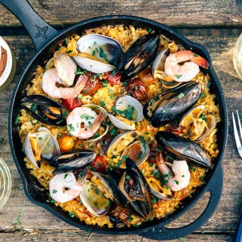 Paella topped with shrimp, mussels, and clams in a cast iron skillet on a camp table
