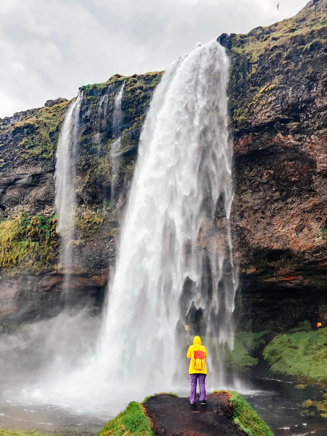 Woman in a yellow raincoat standing in front of the Seljalandsfoss waterfall