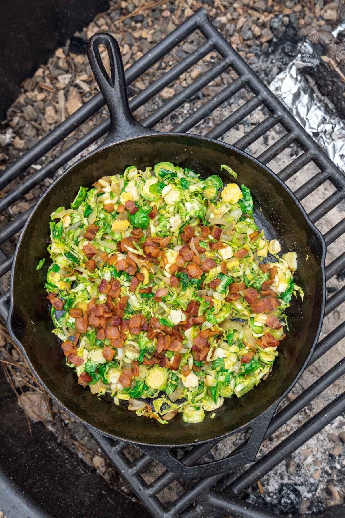 Brussels sprouts and bacon in a cast iron skillet over a campfire