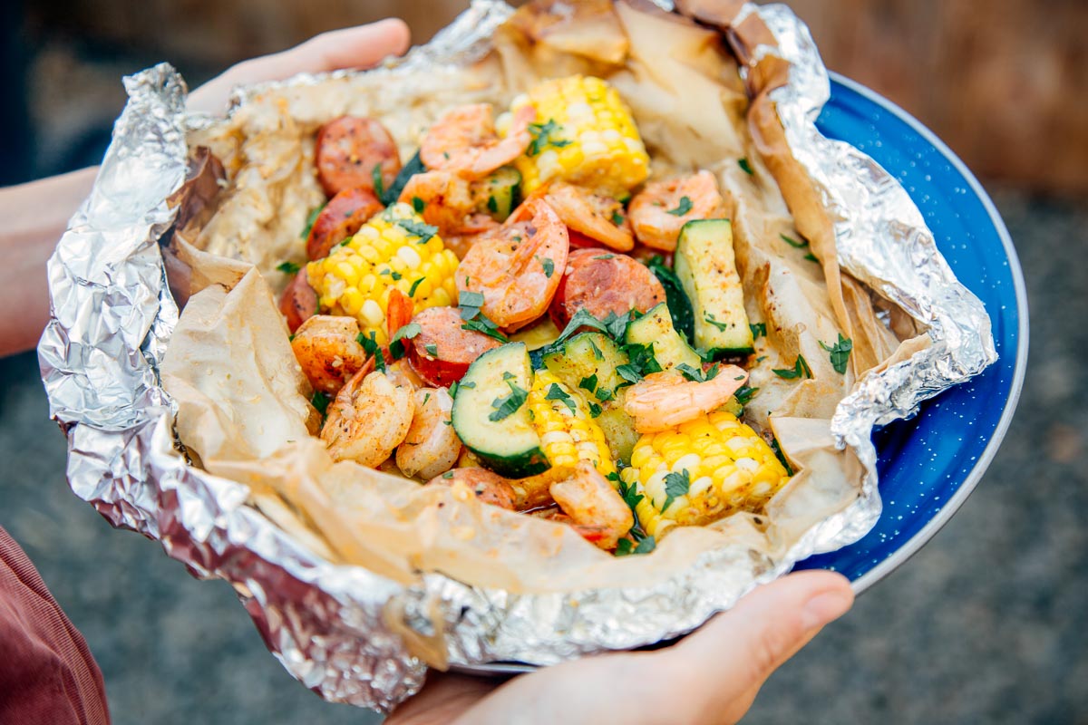 Woman holding a shrimp boil foil packet on a blue plate