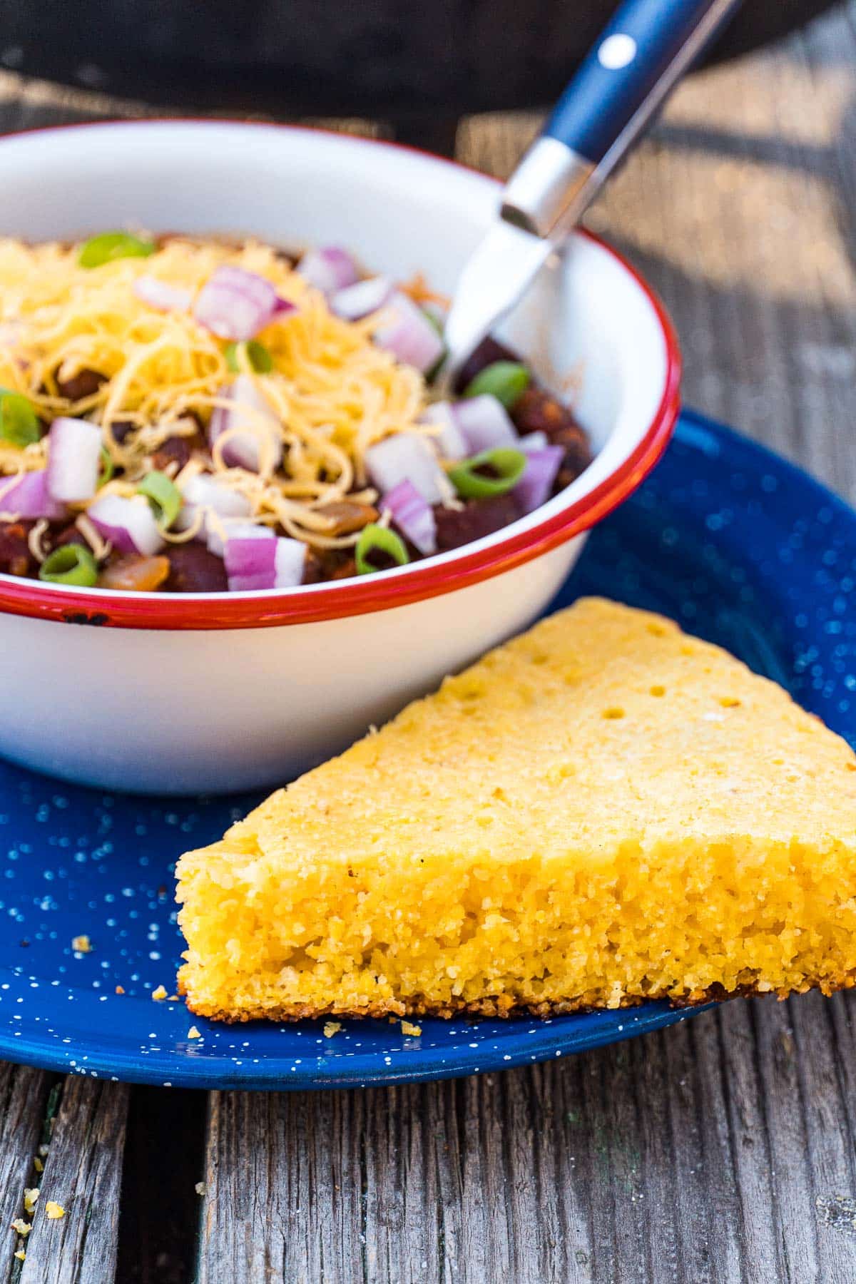 A slice of cornbread on a plate with a bowl of chili