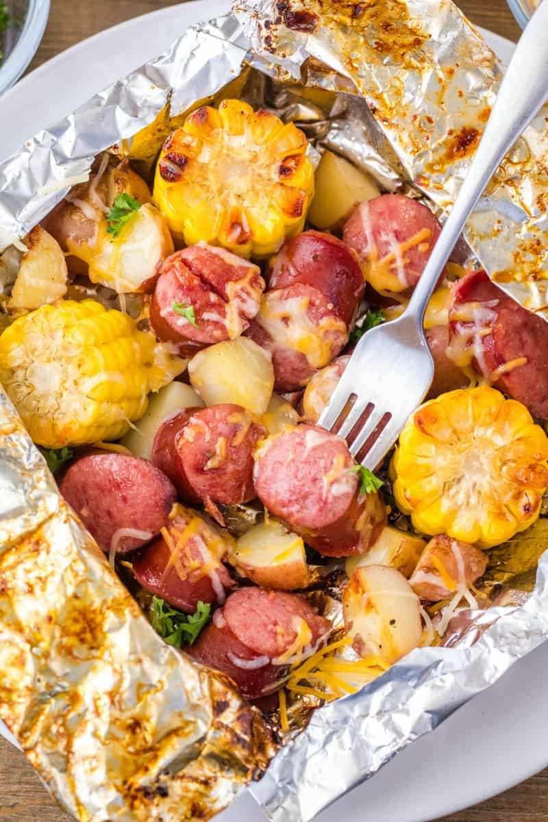 Slices of sausage, corn on the cob, and potatoes in foil.