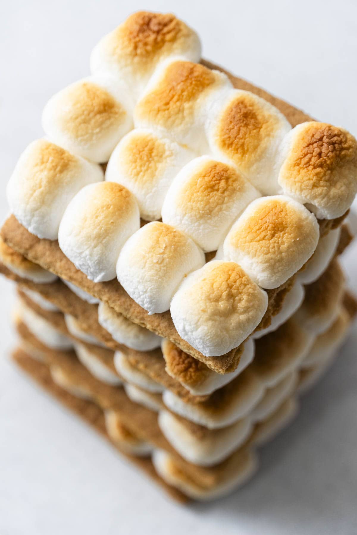 A close-up shows stacked graham crackers with toasted mini marshmallows neatly arranged in rows on a light background.