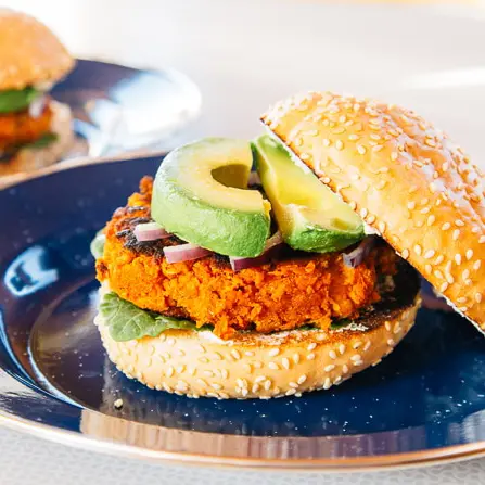 Sweet potato bean burger topped with avocado on a blue blate