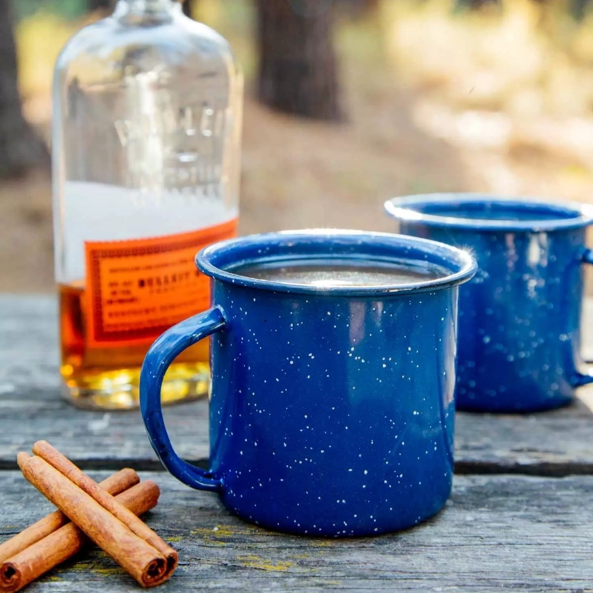 A blue enamel mug next to a bottle of whiskey