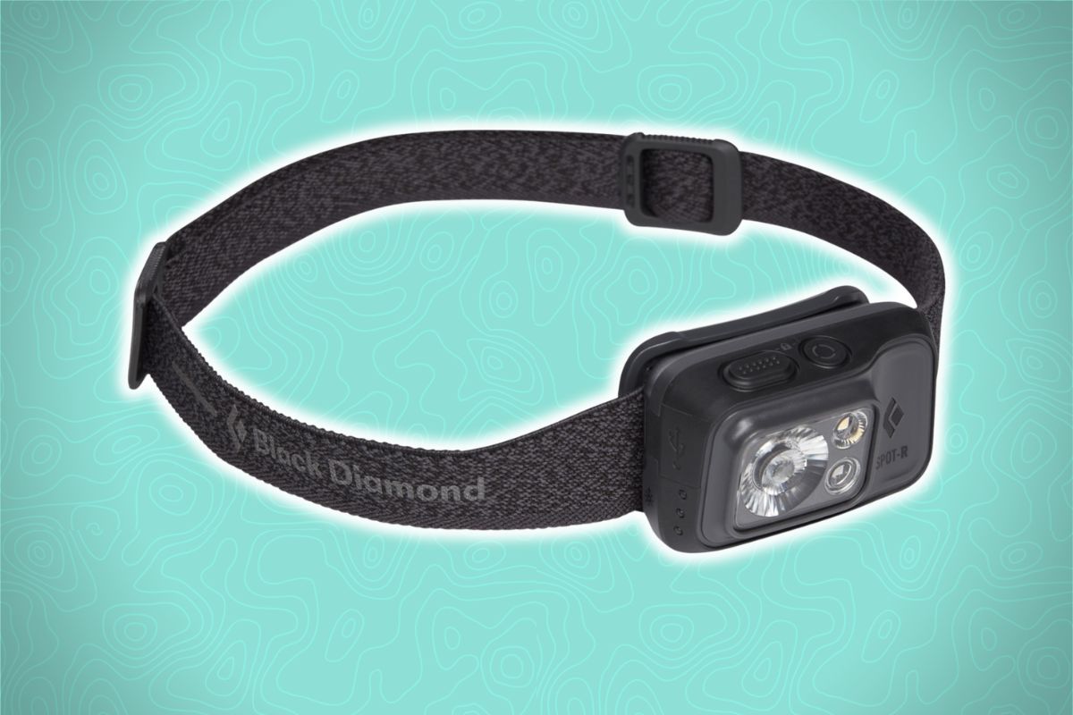 A black Black Diamond headlamp with an adjustable strap, two bulbs, and a button rests on a light blue background with map patterns.