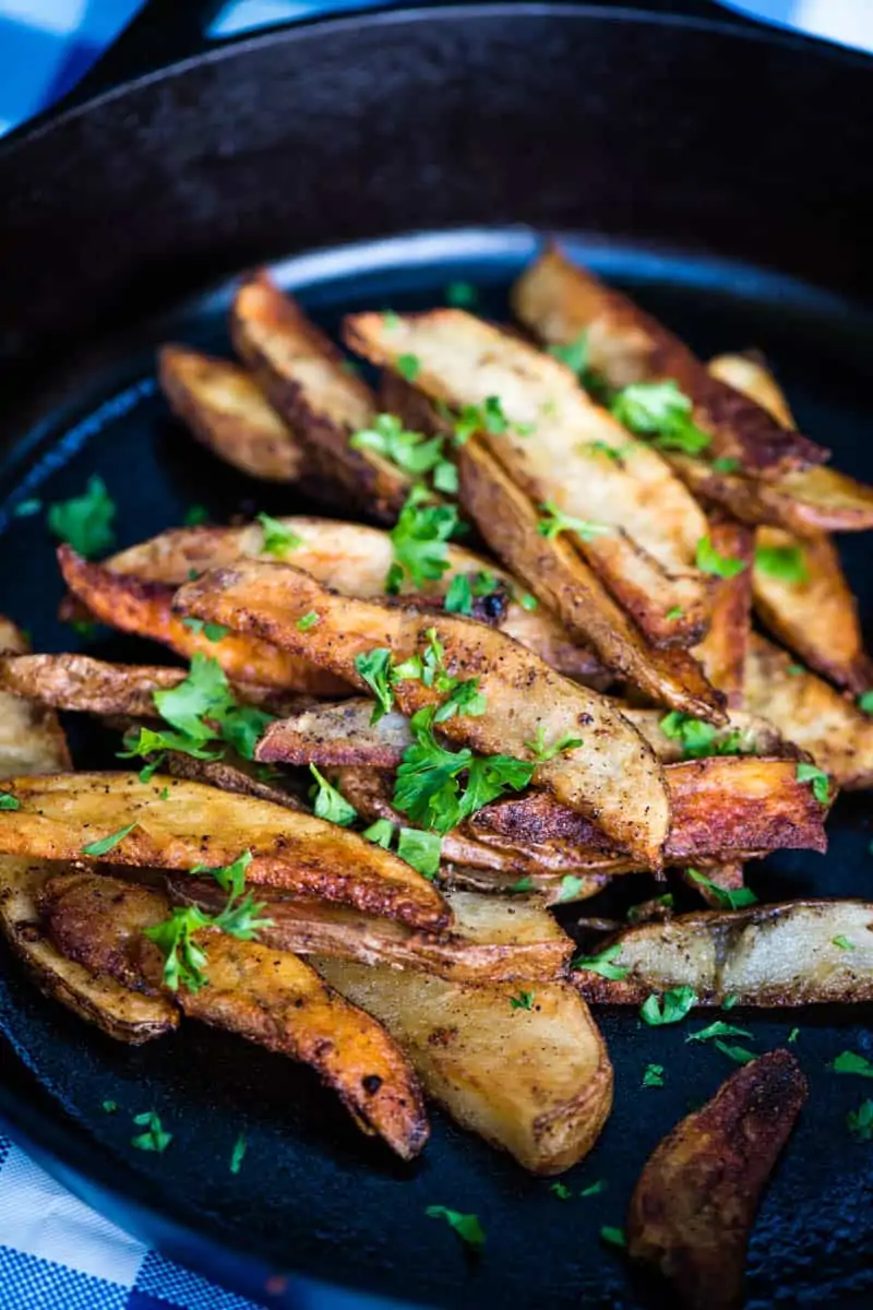 A skillet holds garnished potato wedges atop a blue-striped cloth.