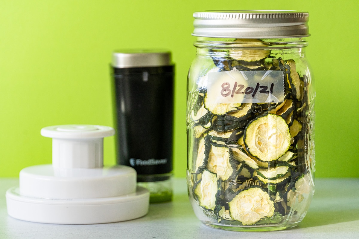 Zucchini chips in a mason jar with a handheld vaccum sealer in the background