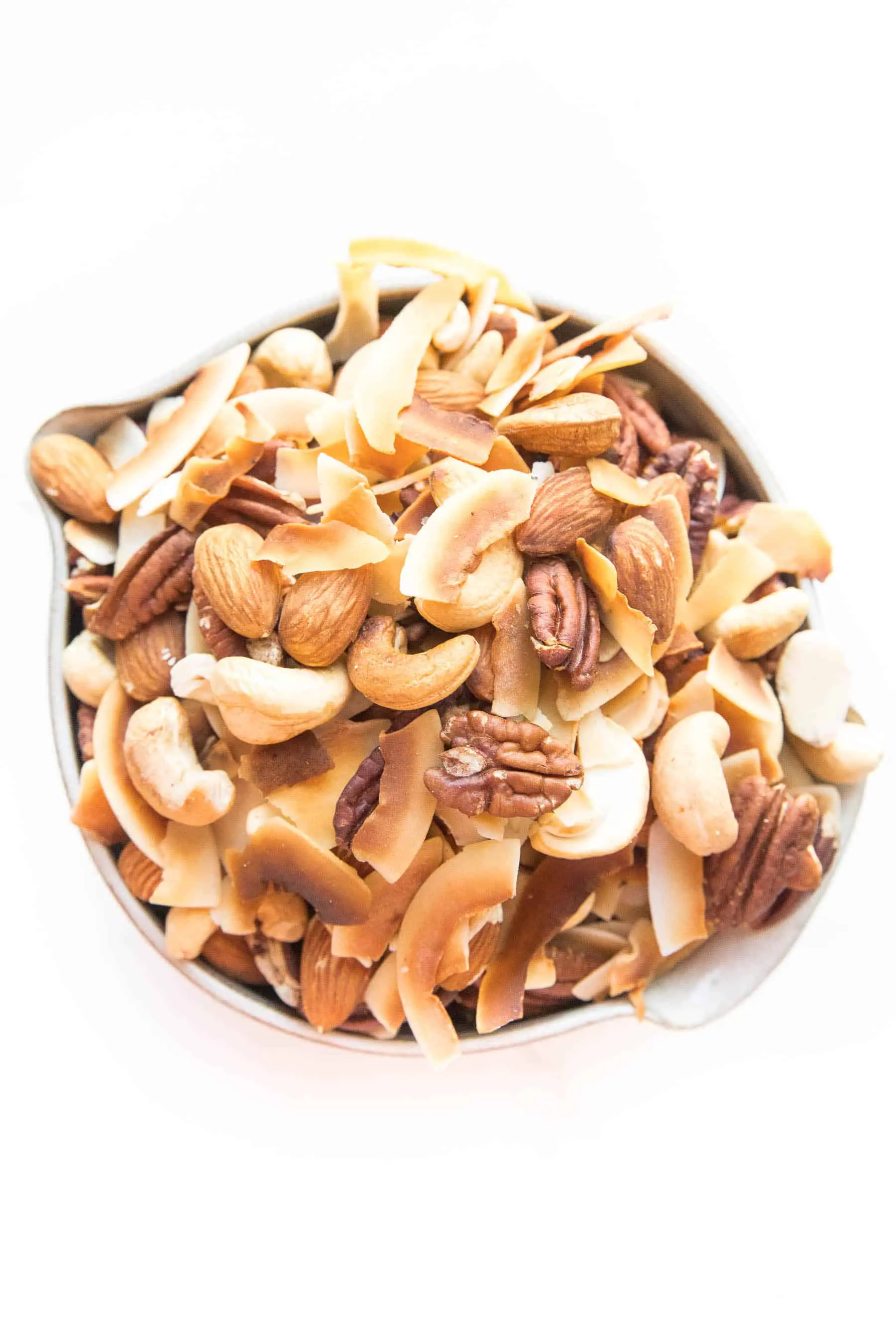 Assorted nuts and coconut chips in a bowl on a white surface