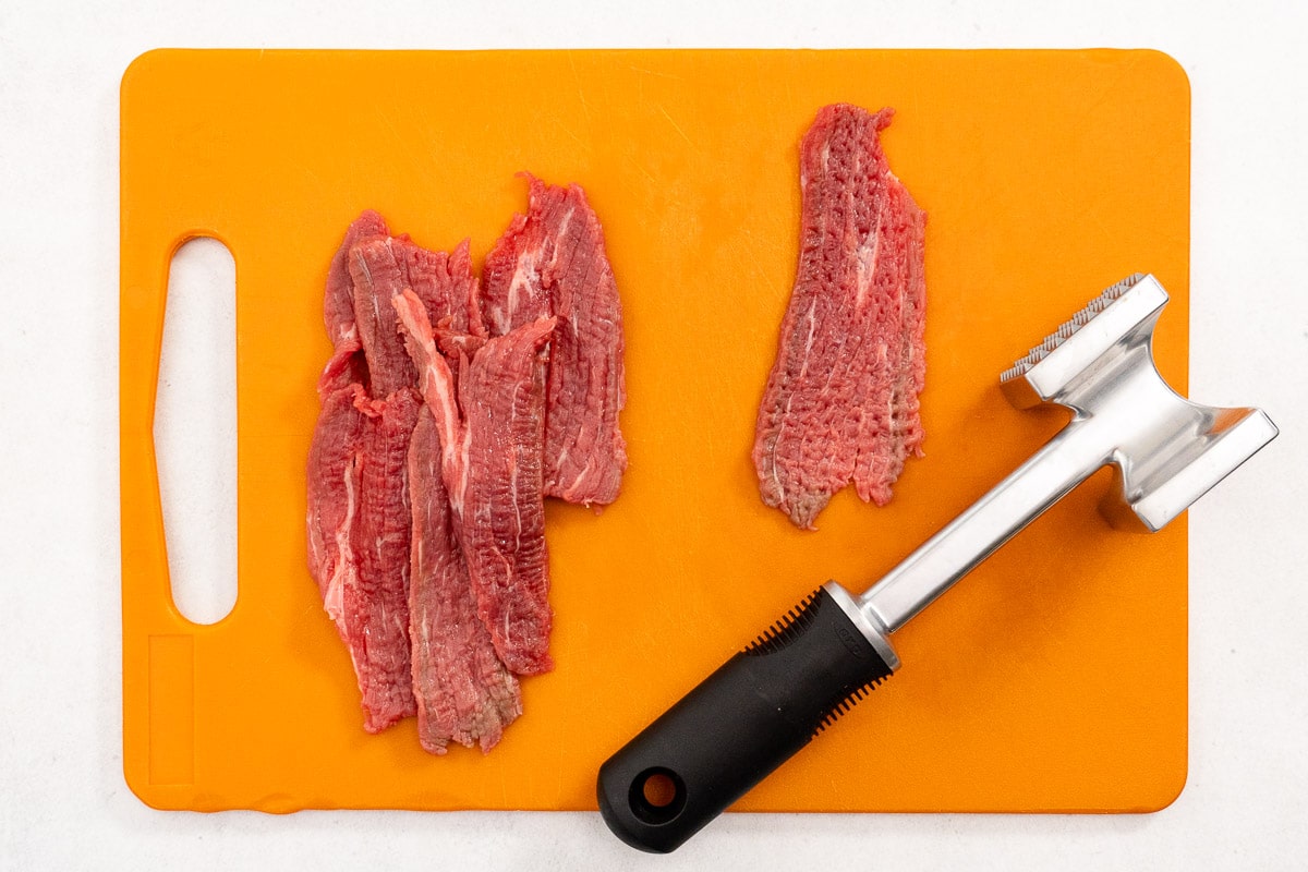 Sliced beef and a mallet on an orange cutting board