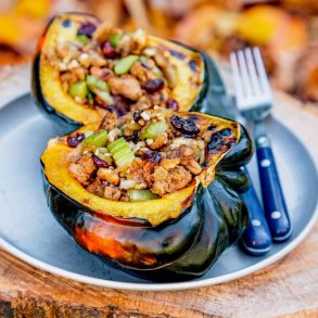 Half acorn squash filled with stuffing on slabs with leaves in the background