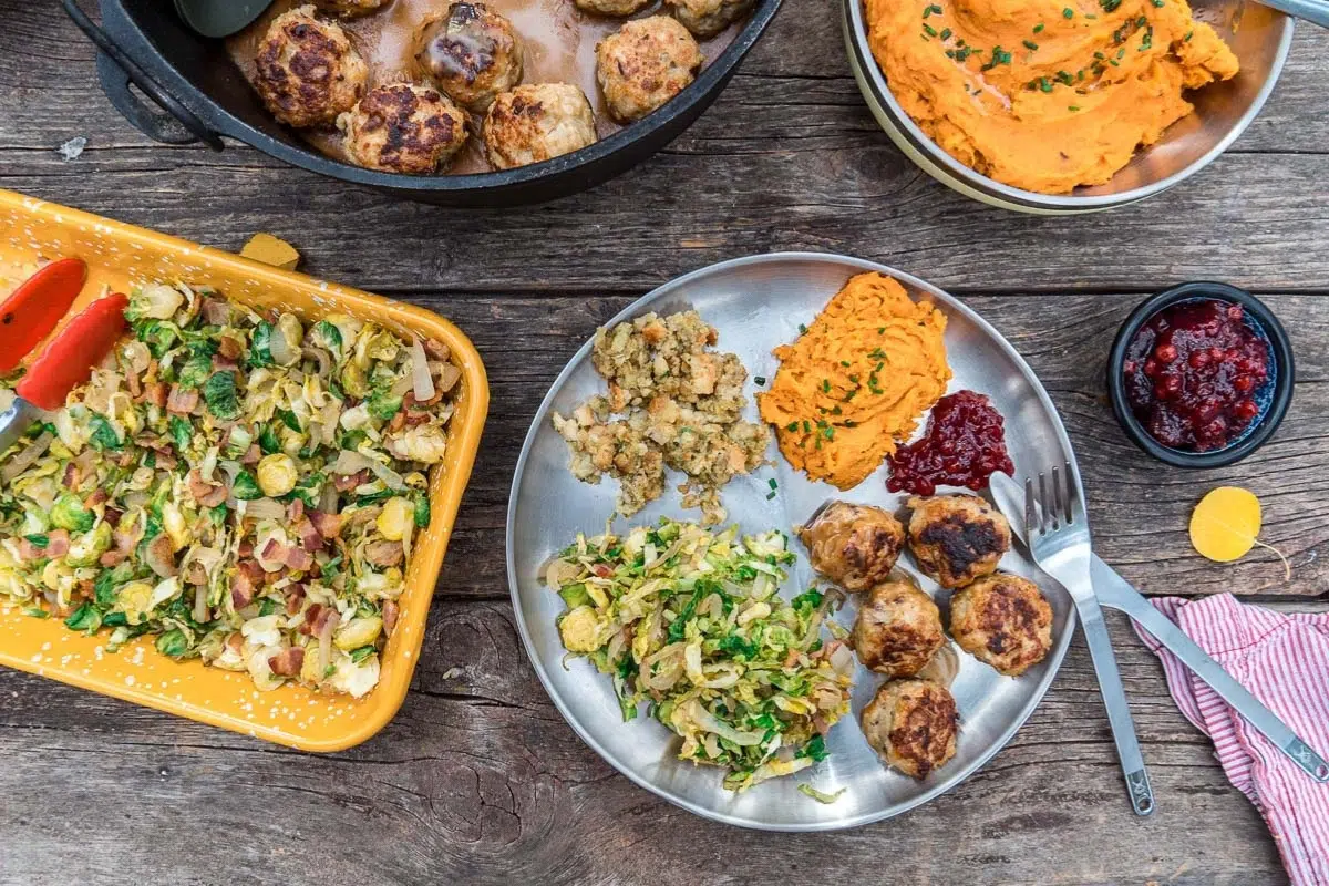 A plate filled with meatballs, brussels sprouts, and sweet potatoes on a table surrounded by serving dishes