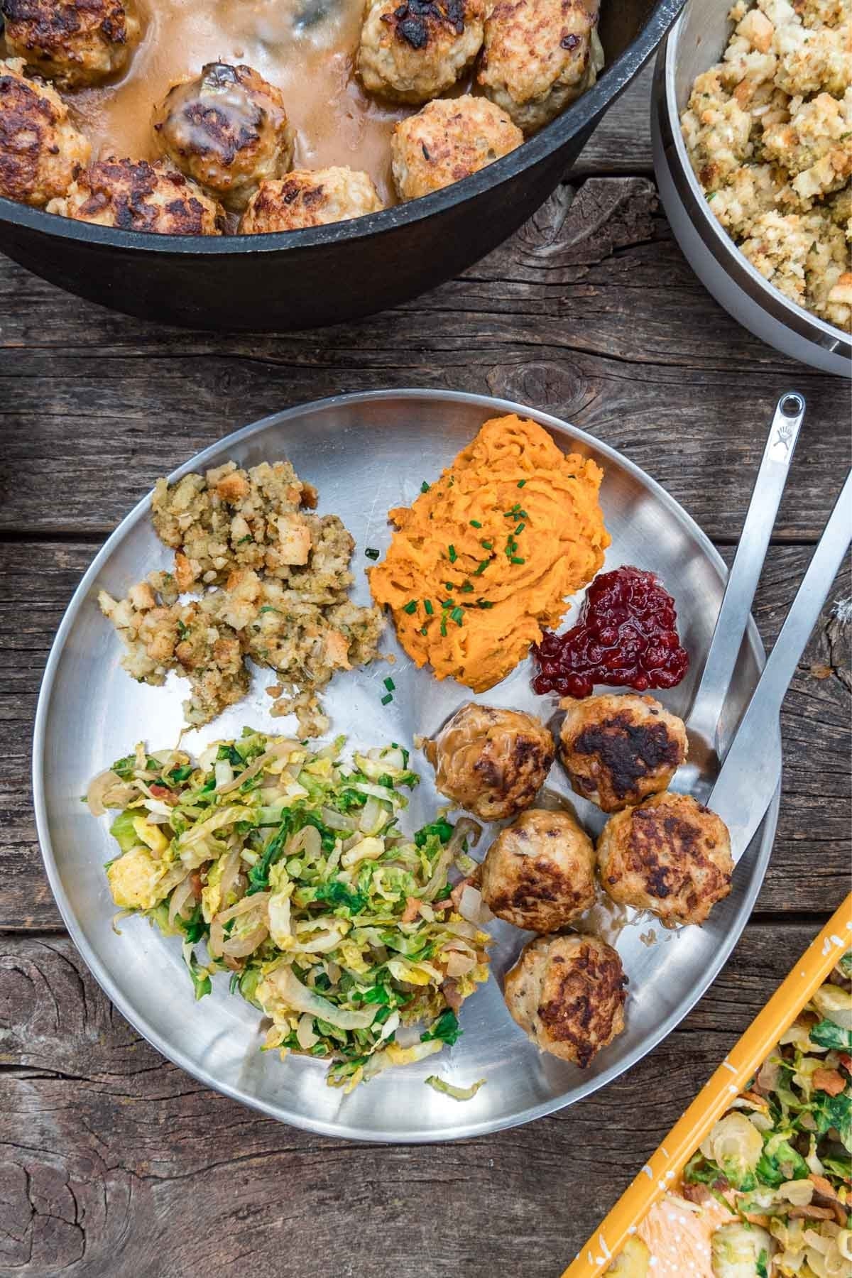 A plate filled with meatballs, brussels sprouts, and sweet potatoes on a table surrounded by serving dishes