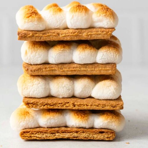 Four s'mores stacked with toasted marshmallows and graham crackers on a light-colored surface.