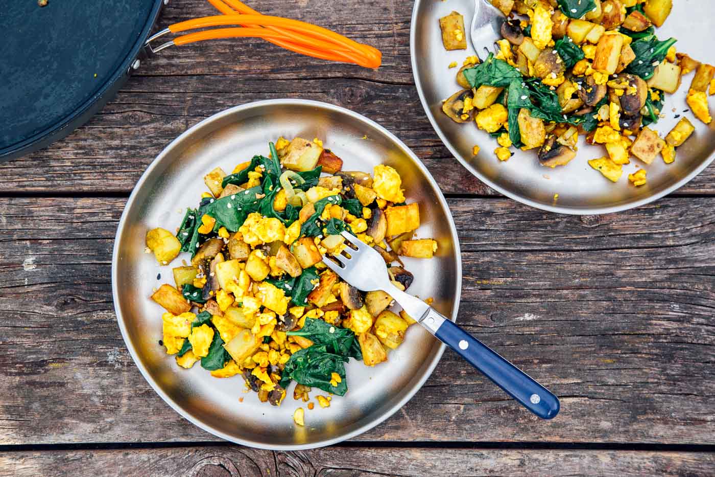 Overhead photo of tofu scramble with spinach on two silver camping plates.