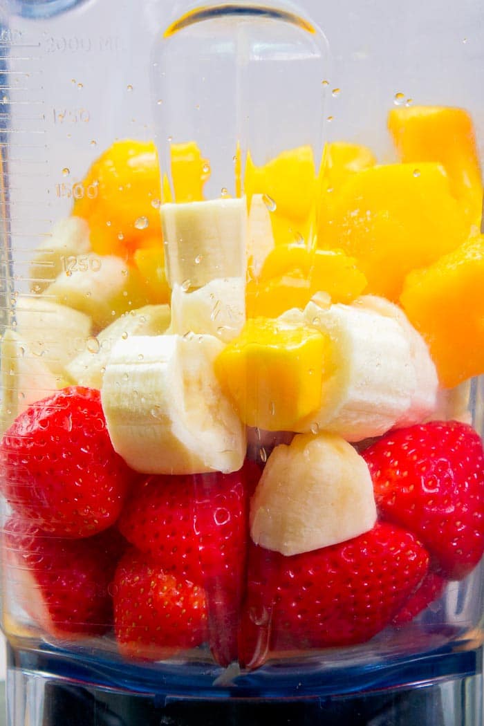 Cut up strawberries, mangoes, and bananas in a blender.