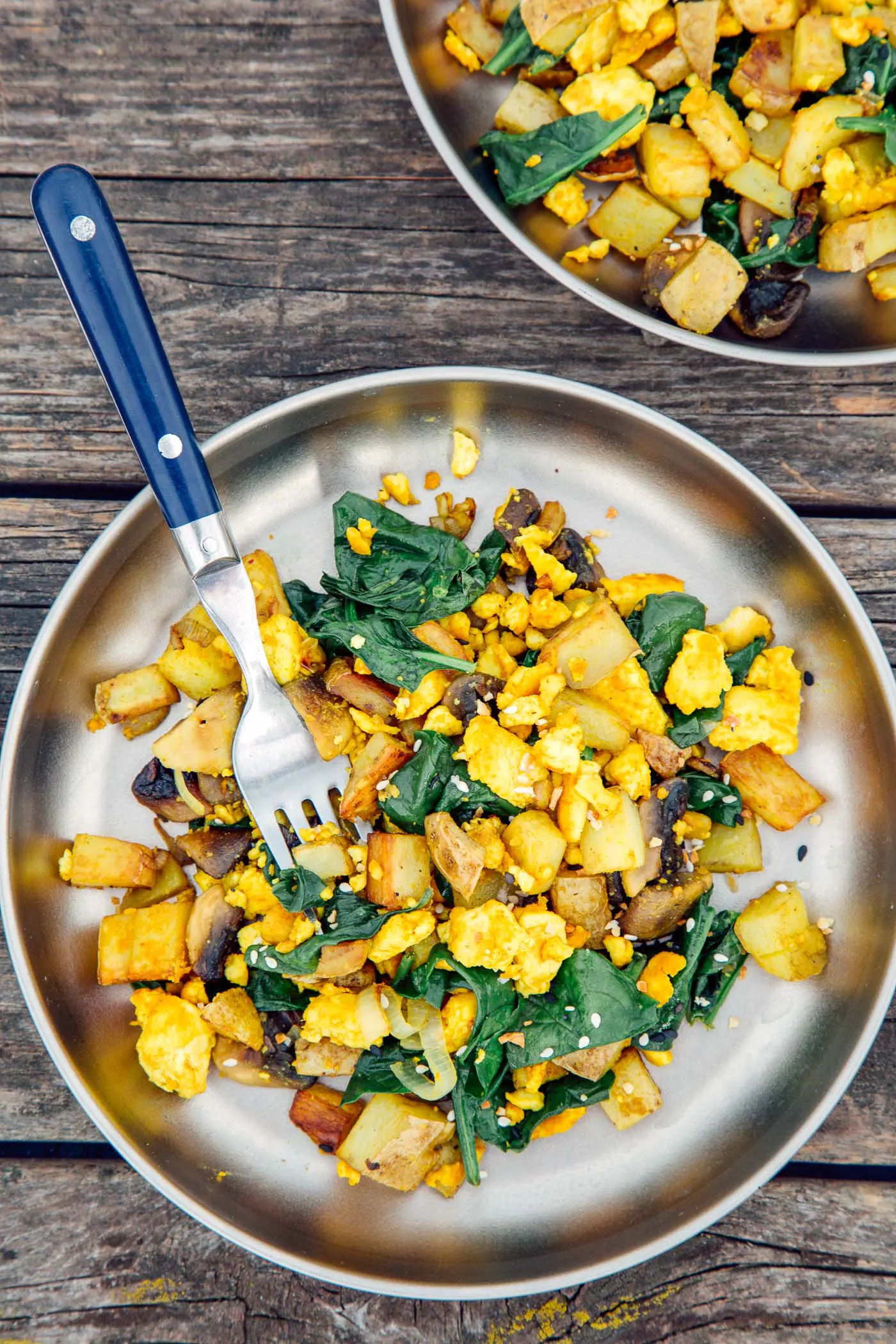 Overhead vertical photo of tofu scramble with spinach on two silver camping plates.