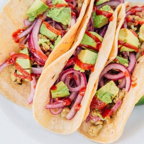 Three cauliflower tacos topped with avocado and red onions