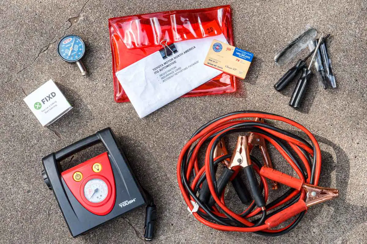Overhead view of jumper cables, tire patch kit, tire pressure guage, and a tire inflator