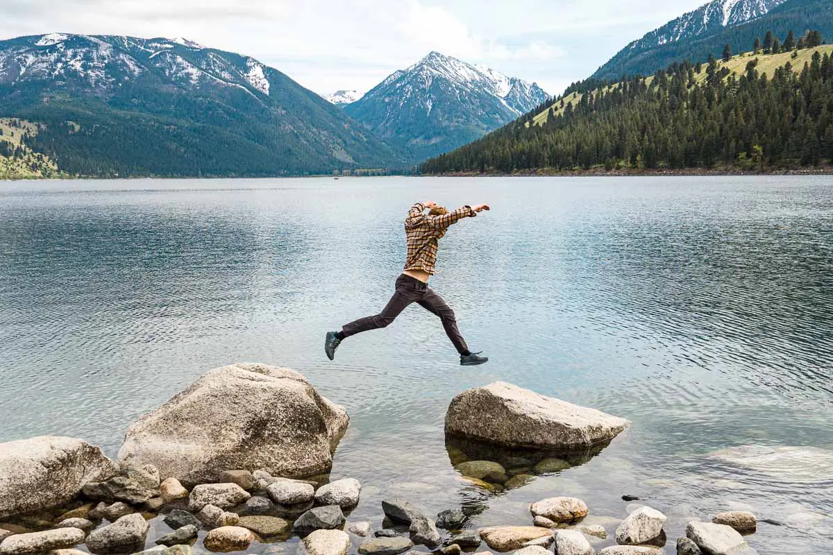 Michael hops between two boulders in Wallowa Lake with the Wallowa Mountains in the background