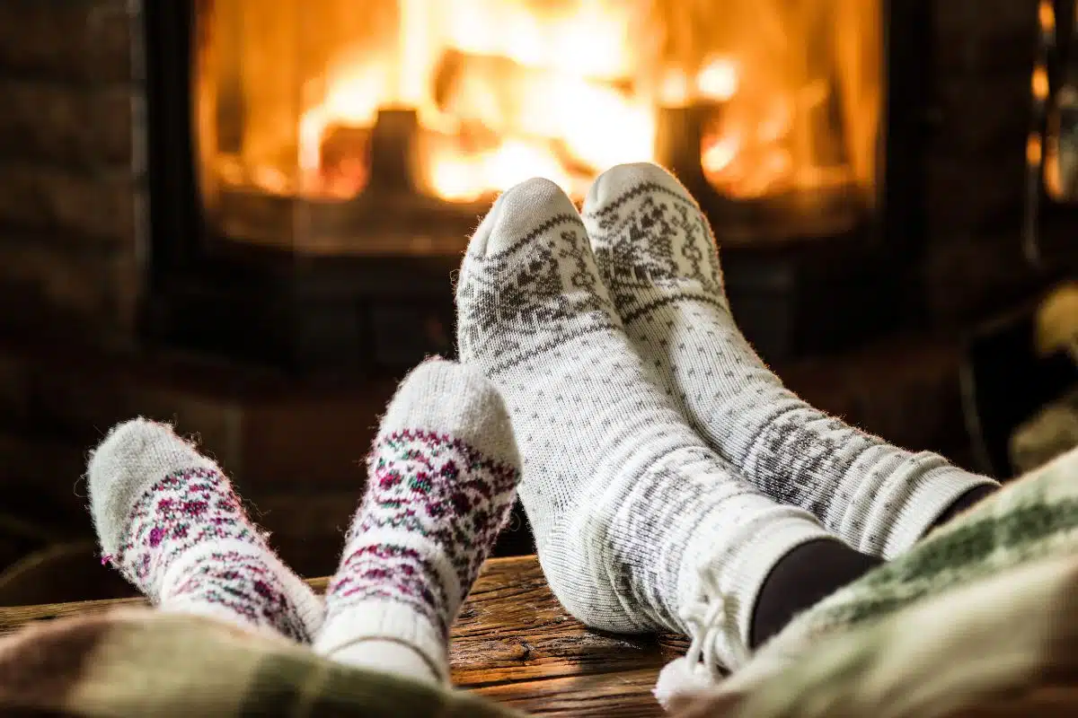 Two pairs of feet wearing warm fuzzy socks with a fireplace in the background.