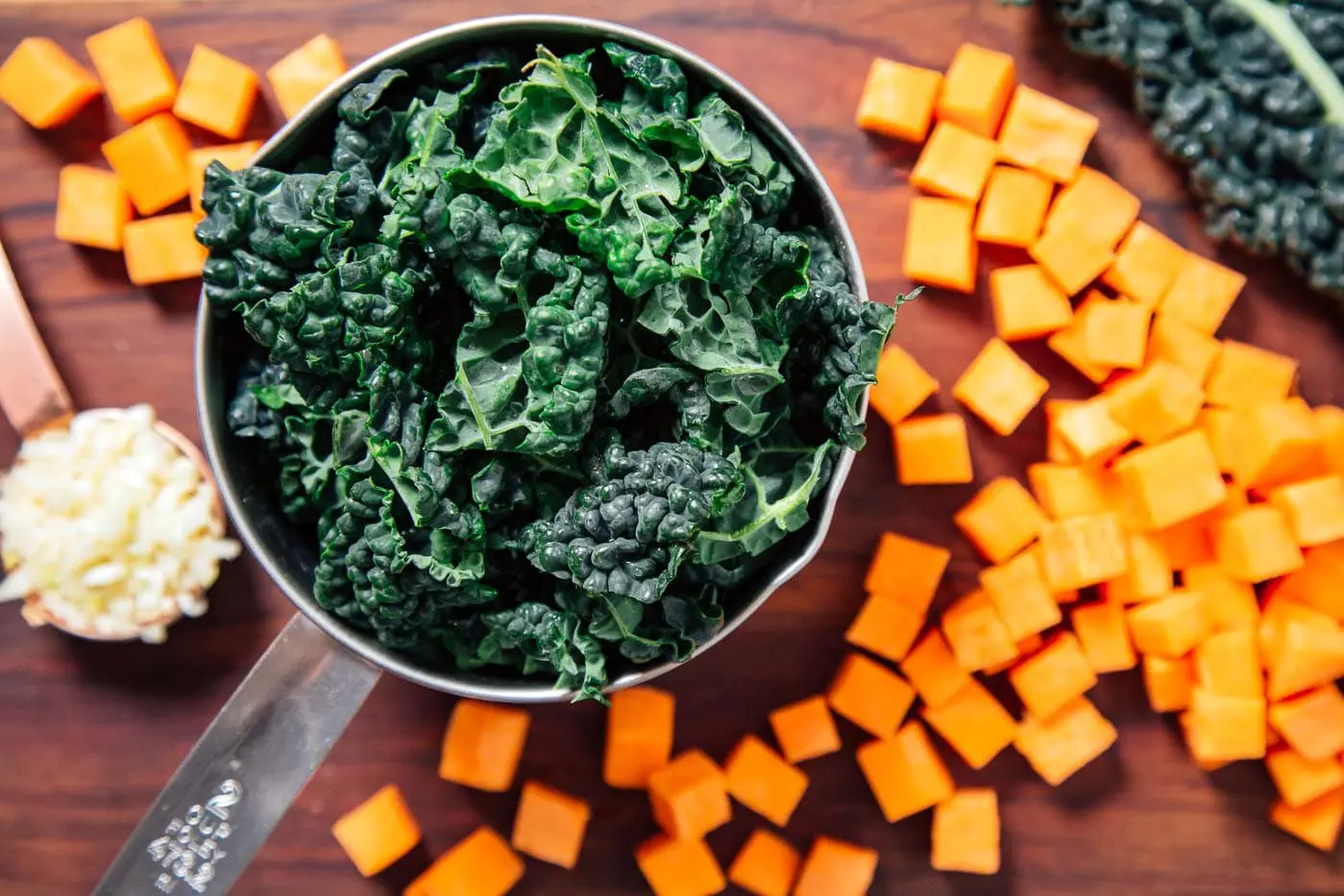 Kale in a measuring cup next to cubed sweet potato on a cutting board