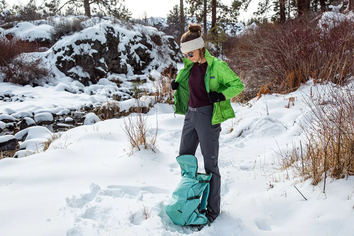 A woman putting on a jacket during a winter hike