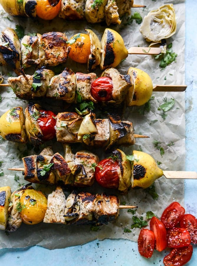 Grilled chicken and vegetable skewers with charred lemon and fresh herbs on parchment paper, ready for a flavorful summer feast.