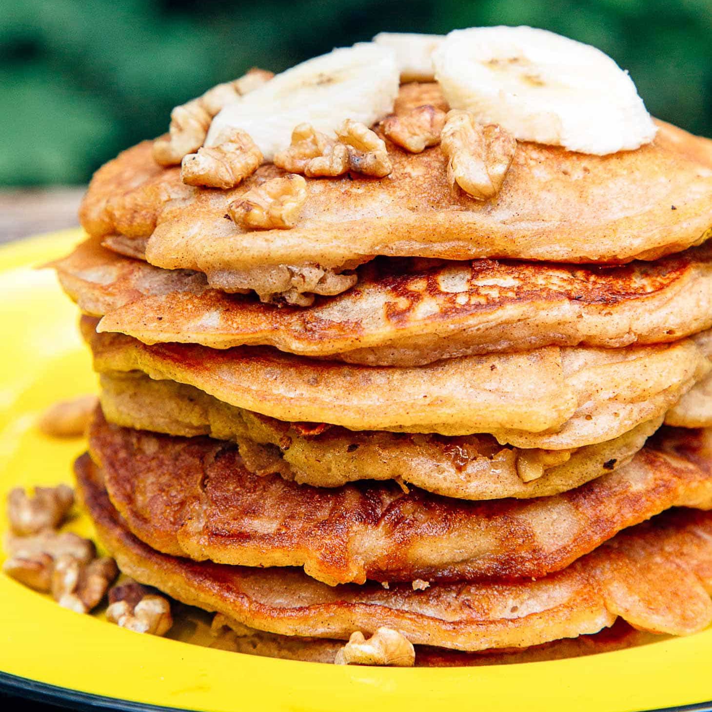 A stack of pancakes topped with sliced bananas on a yellow plate.