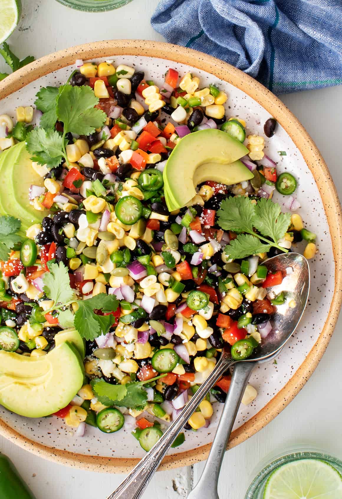 A bowl, vibrant and colorful, holds black beans and corn salad garnished with fresh slices of avocado, jalapeno, and cilantro.