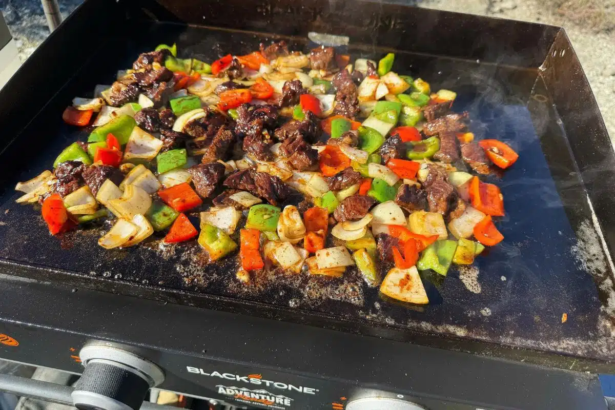 Steak and pepper cooking on a blackstone griddle.