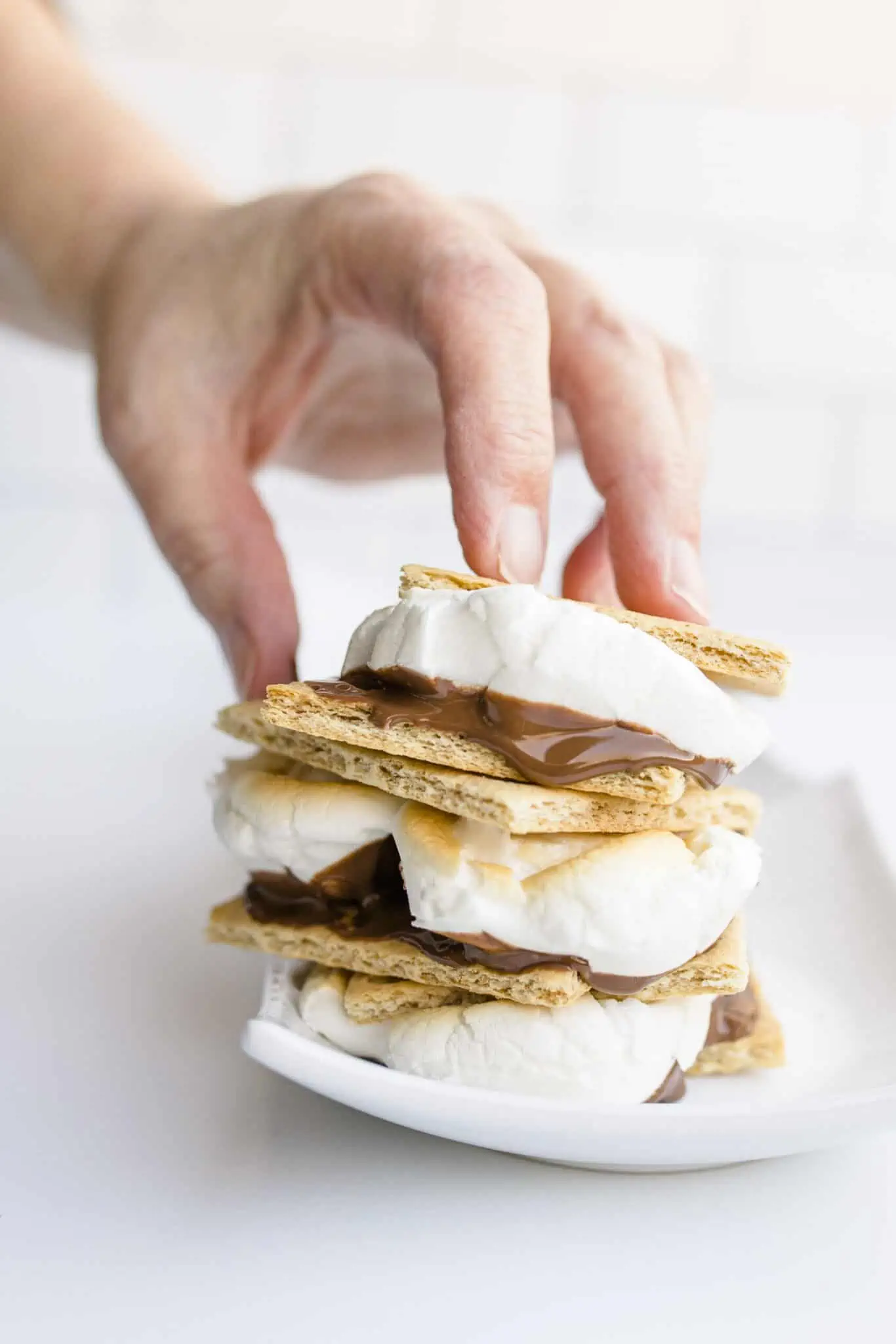 A person using their hand to stack s'mores on a plate.