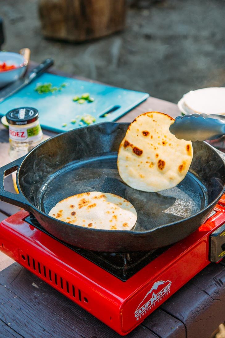 Tongs flipping a tortilla in a skillet