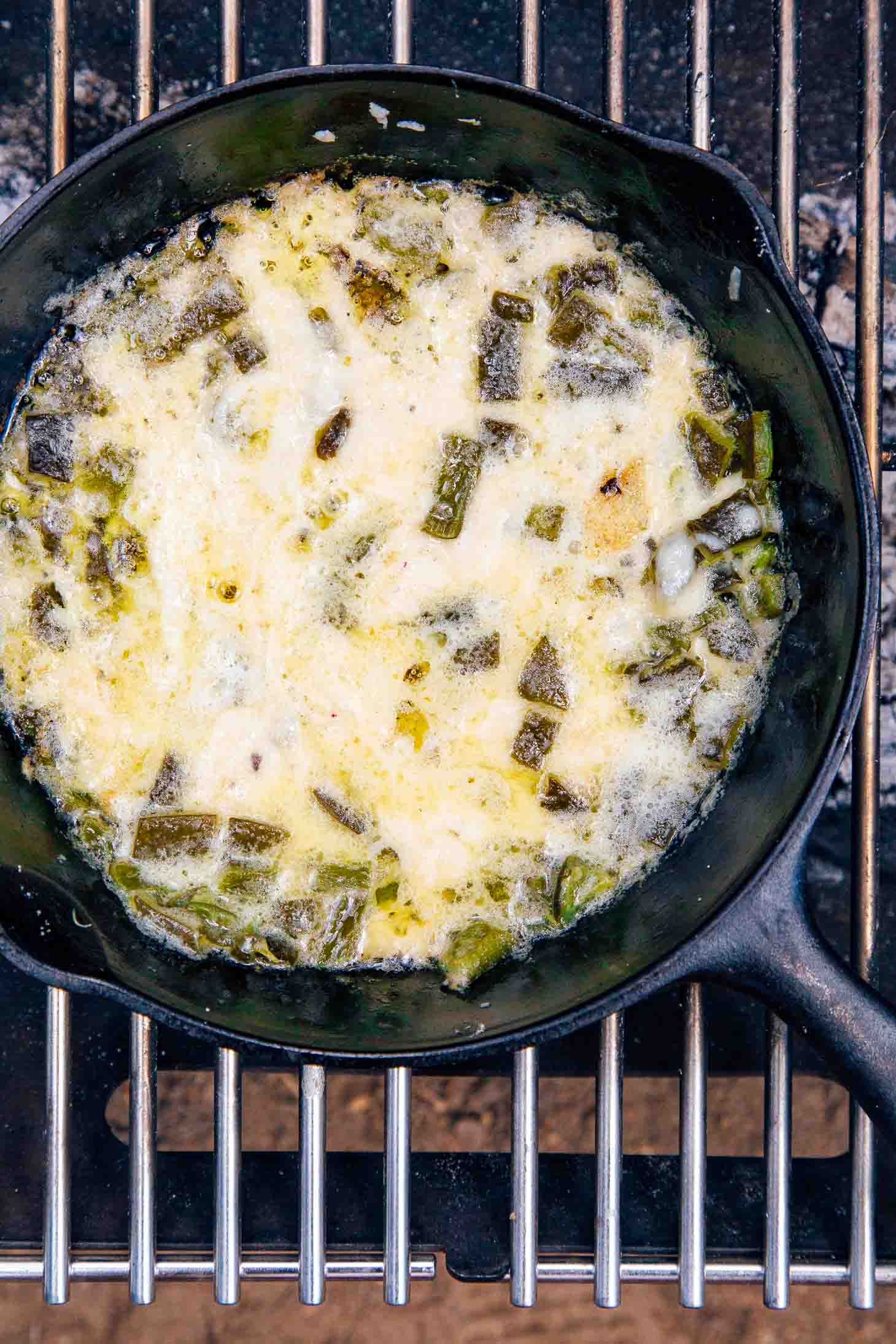 Queso fundido in a cast iron skillet on a campfire grill