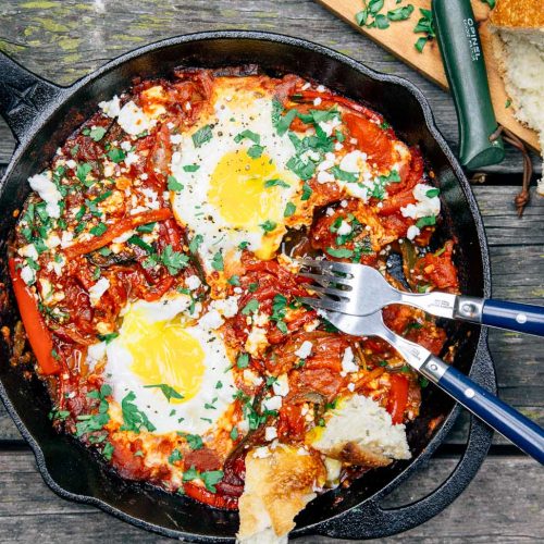 Shakshuka in a cast iron skillet with two eggs and bread