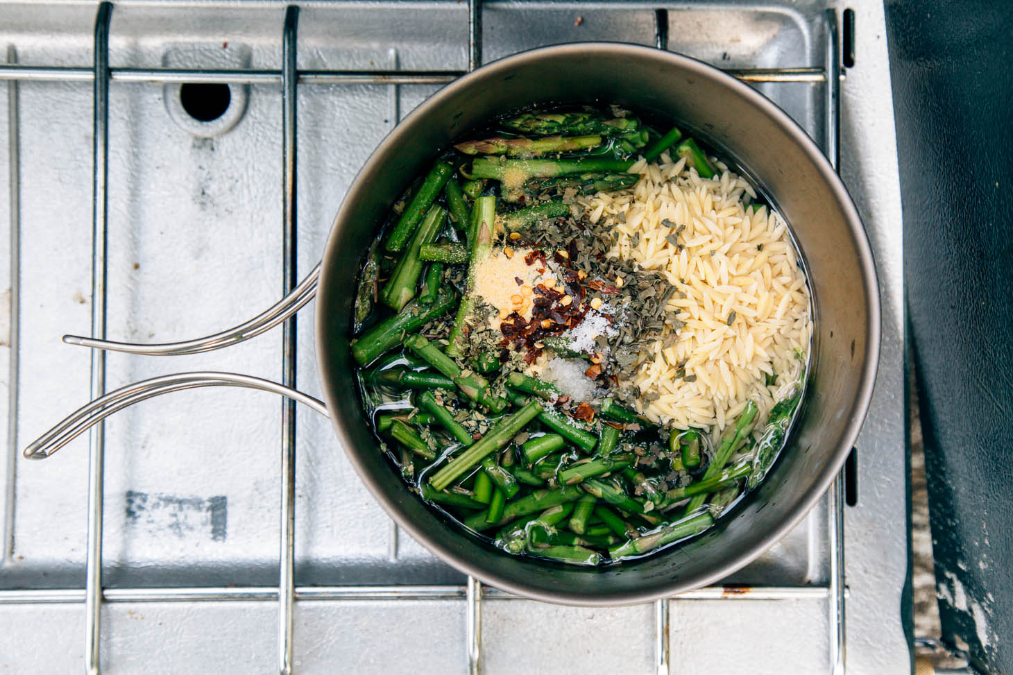 Ingredients for asparagus orzo in a cooking pot on a camping stove