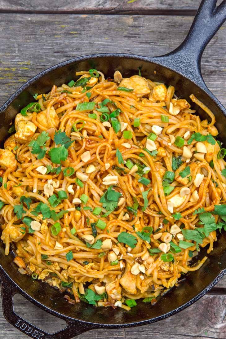 Chicken pad thai in a skillet on a wooden surface
