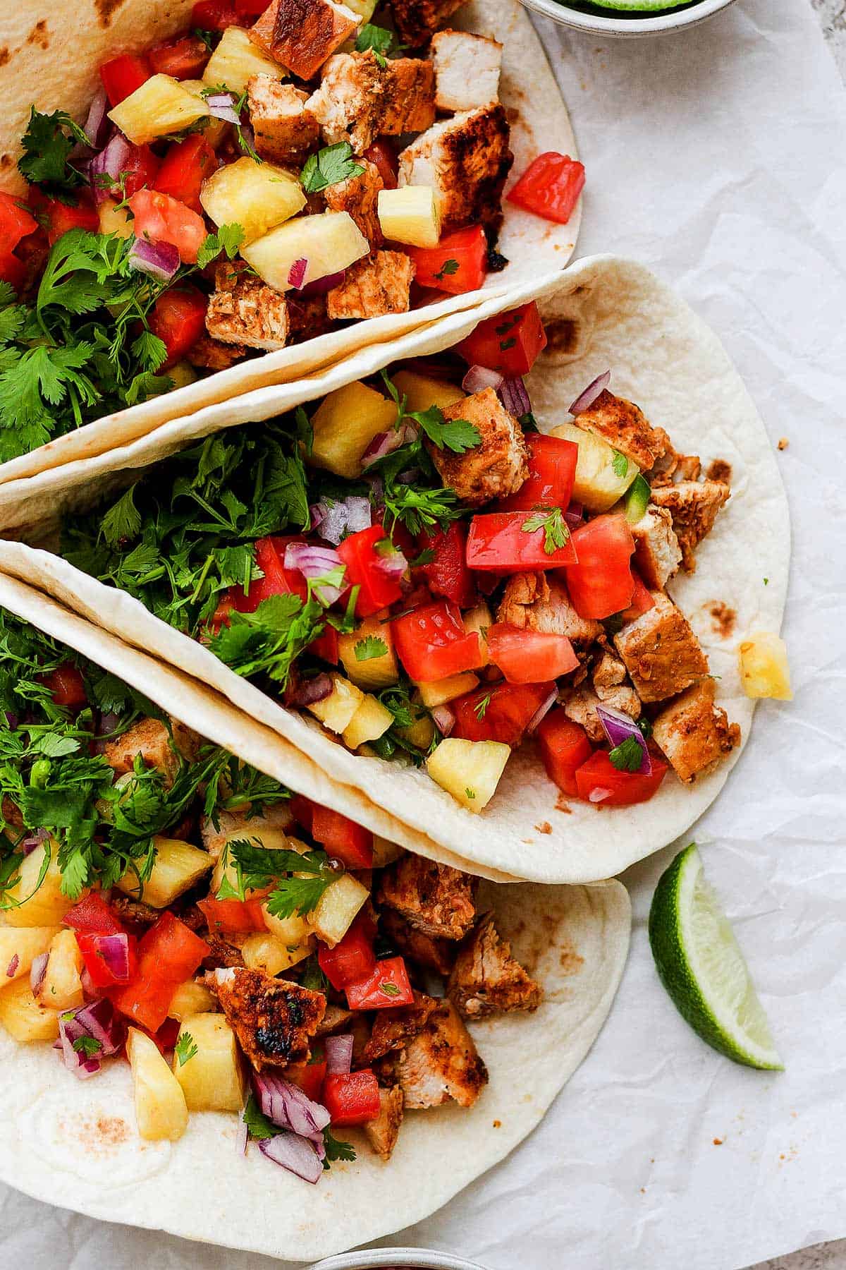 Three chicken tacos garnished with pineapple salsa and fresh cilantro are served in soft tortillas.