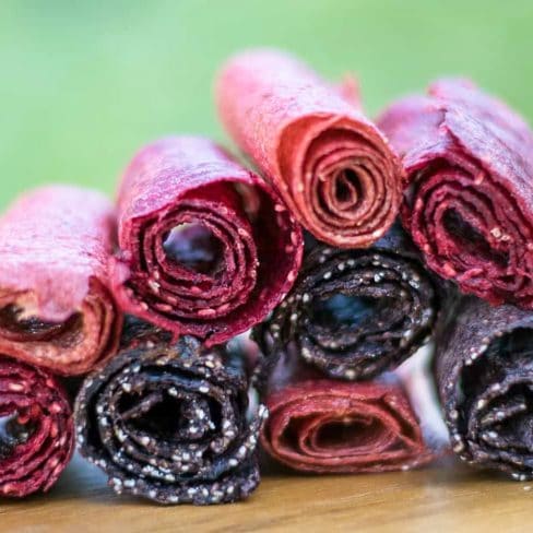A close-up of vibrant, homemade fruit leather rolls in red and dark purple colors, suggesting a tasty and natural snack option.