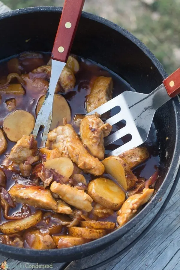 Chicken, potatoes, and BBQ sauce in a dutch oven with serving utensils