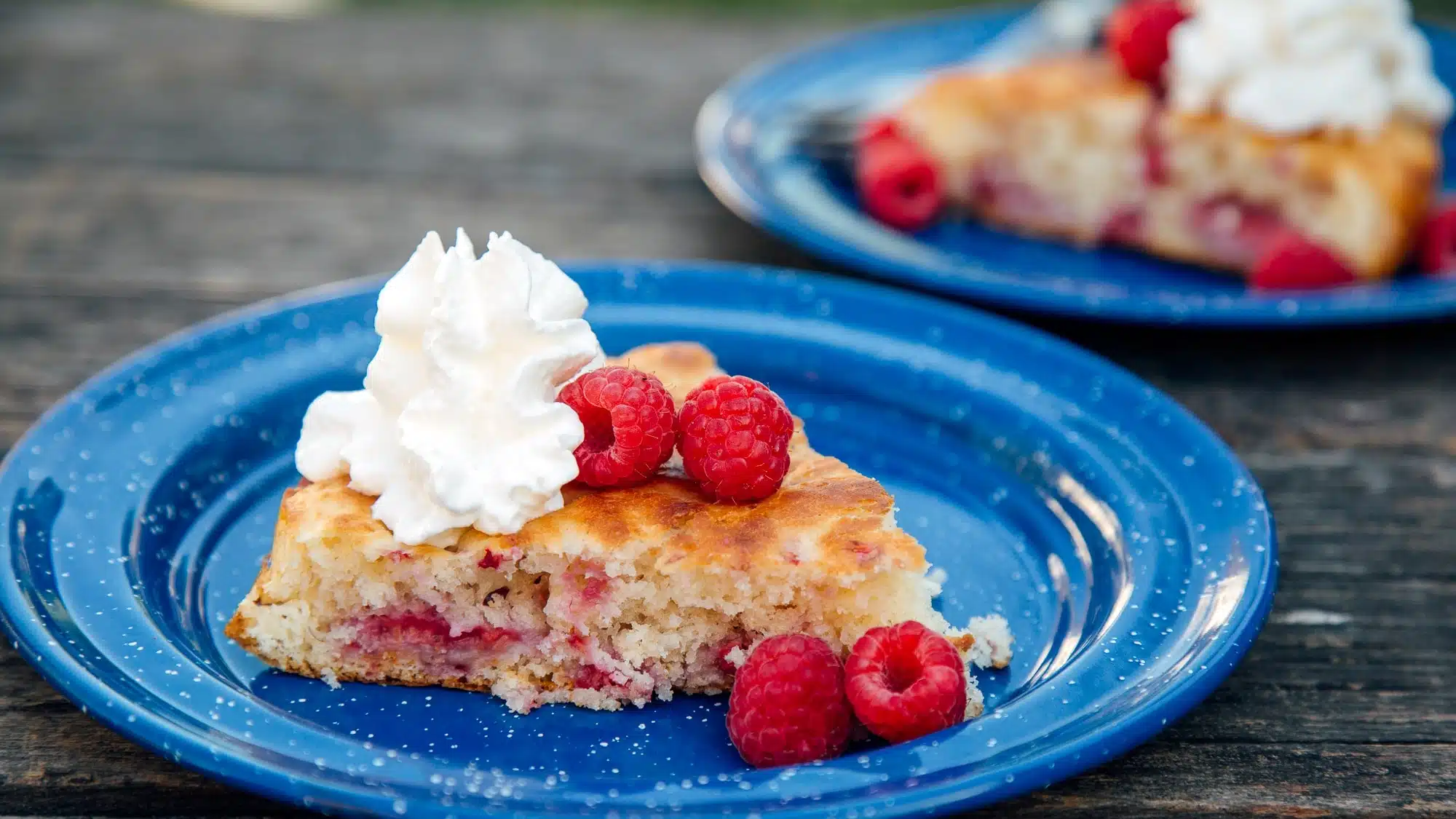 A slice of cake topped with whipped cream and whole raspberries.
