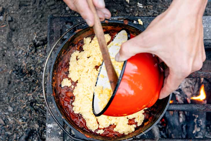 Pouring cornbread batter over chili in a Dutch oven