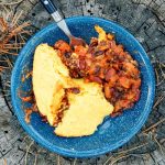 A bowl of chili and cornbread on a tree stump