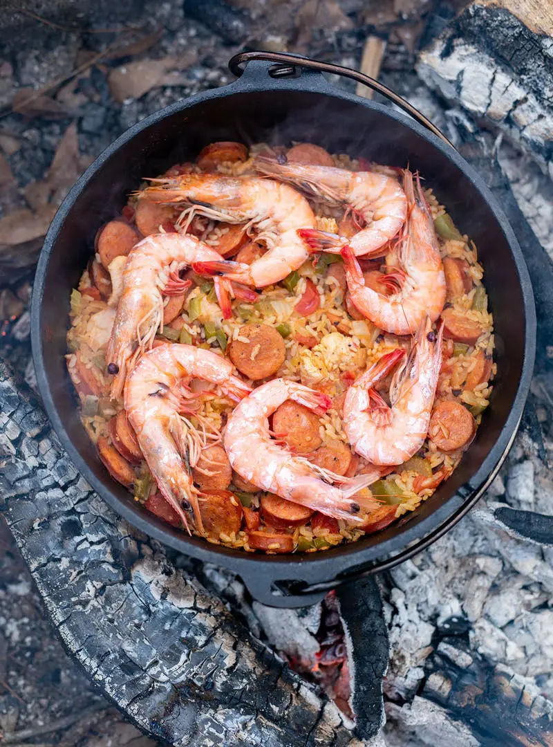 Jambalaya topped with seven large shrimp in a Dutch oven over coals