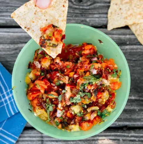 A hand dipping a tortilla chip into a colorful bowl of fresh salsa.
