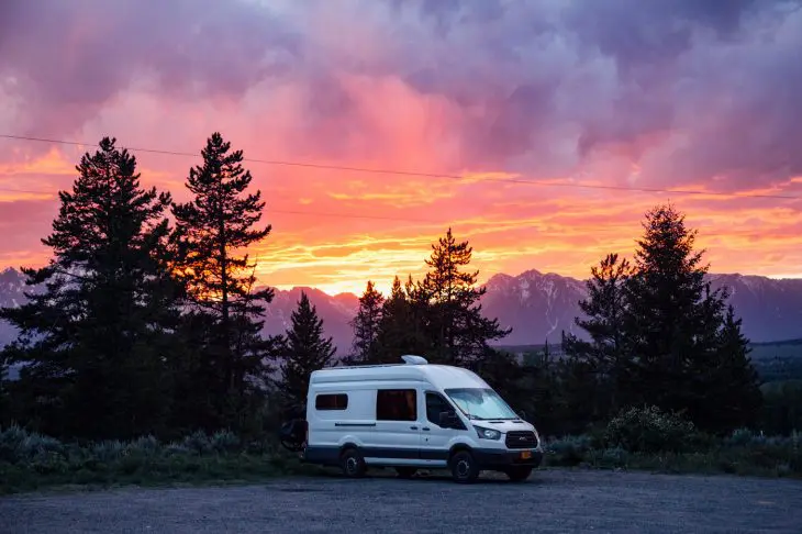 A campervan parked with a sunset and the Teton mountains in the background