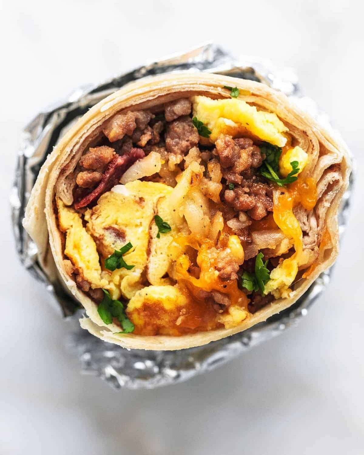 A foil-wrapped breakfast burrito filled with eggs, sausage, beans, and cheese.